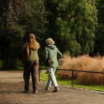 Duas pessoas caminham por um parque arborizado durante o dia.