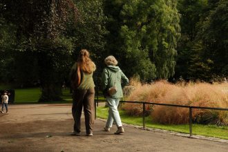 Duas pessoas caminham por um parque arborizado durante o dia.