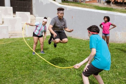Grupo diverso de adolescentes brinca de pular corda ao ar livre em um parque ensolarado.