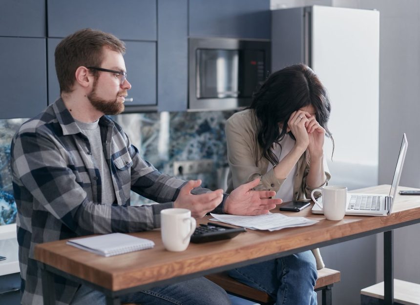 Casal sentado à mesa, com expressão de preocupação, conversando sobre problemas do relacionamento em ambiente doméstico