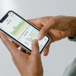 Mãos seguram um smartphone que exibe um aplicativo de acompanhamento de saúde com gráficos e dados.